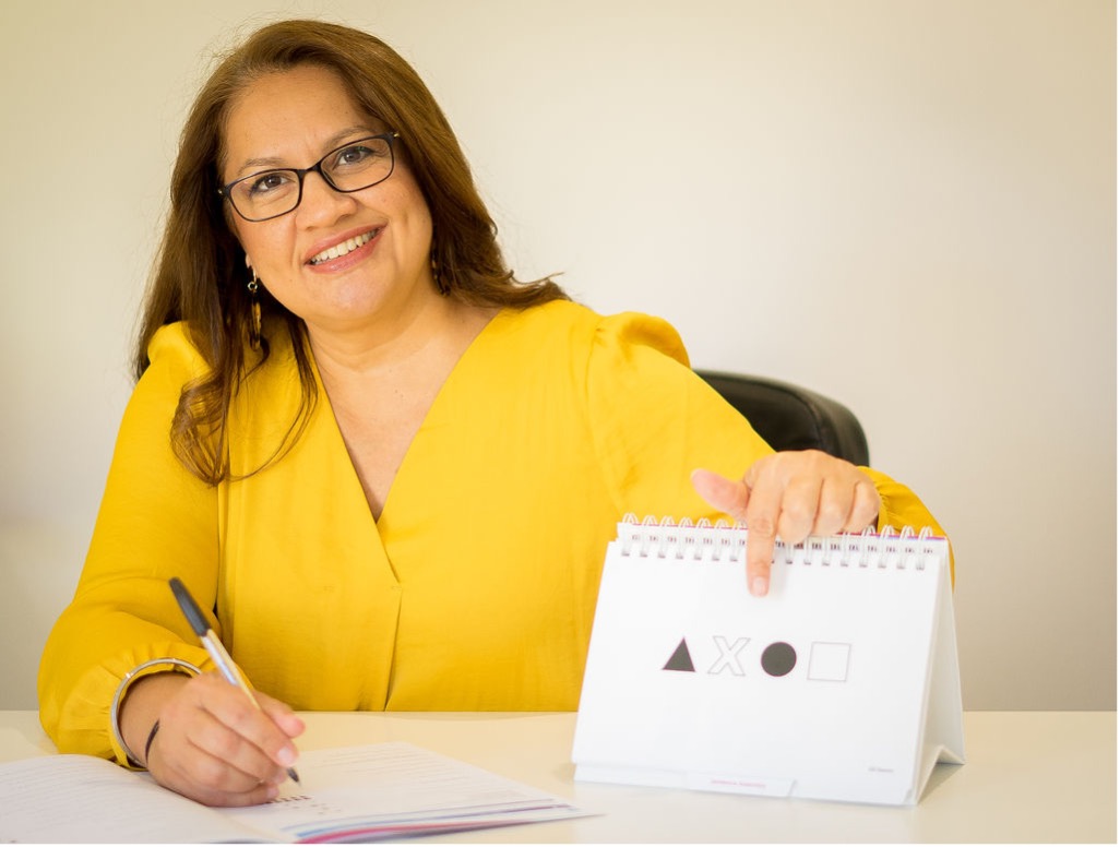 Sim Dhaliwal at her desk, holding a card of shapes and writing session notes